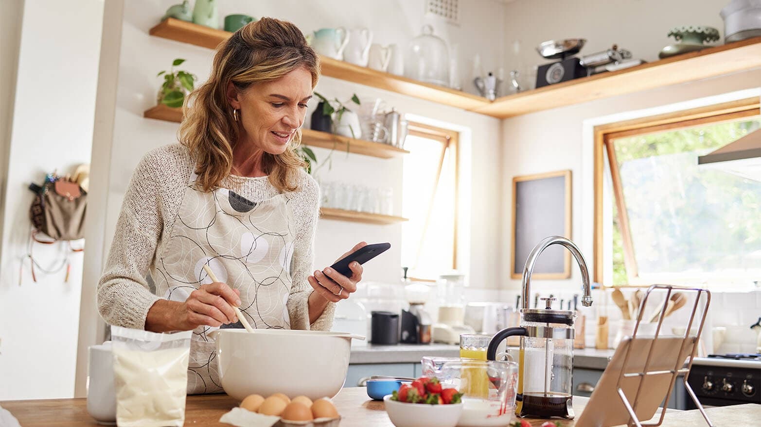 Baking, website and phone with woman cooking food while reading online with blog, internet or app. Kitchen, network and breakfast with chef with web and search recipe for diet, nutrition or lunch